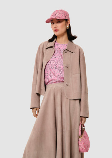 Woman wearing a pink patterned outfit with a beige jacket and skirt, holding a matching pink handbag.