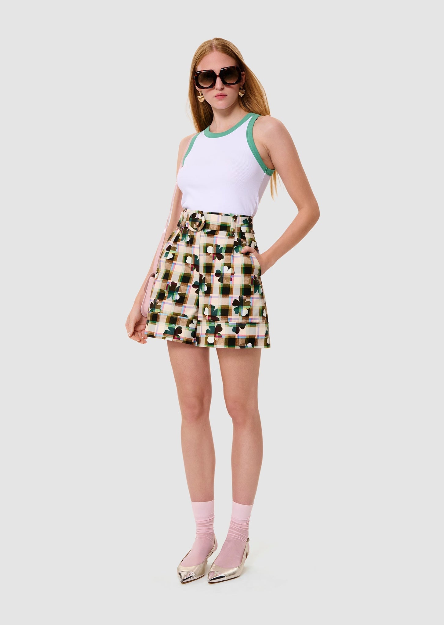 Woman wearing a white tank top with green trim and a floral skirt on a white background