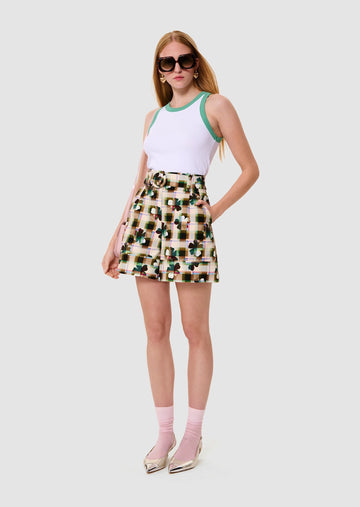 Woman wearing a white tank top with green trim and a floral skirt on a white background