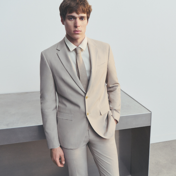 Man wearing a celio light gray suit with a white shirt and striped tie.