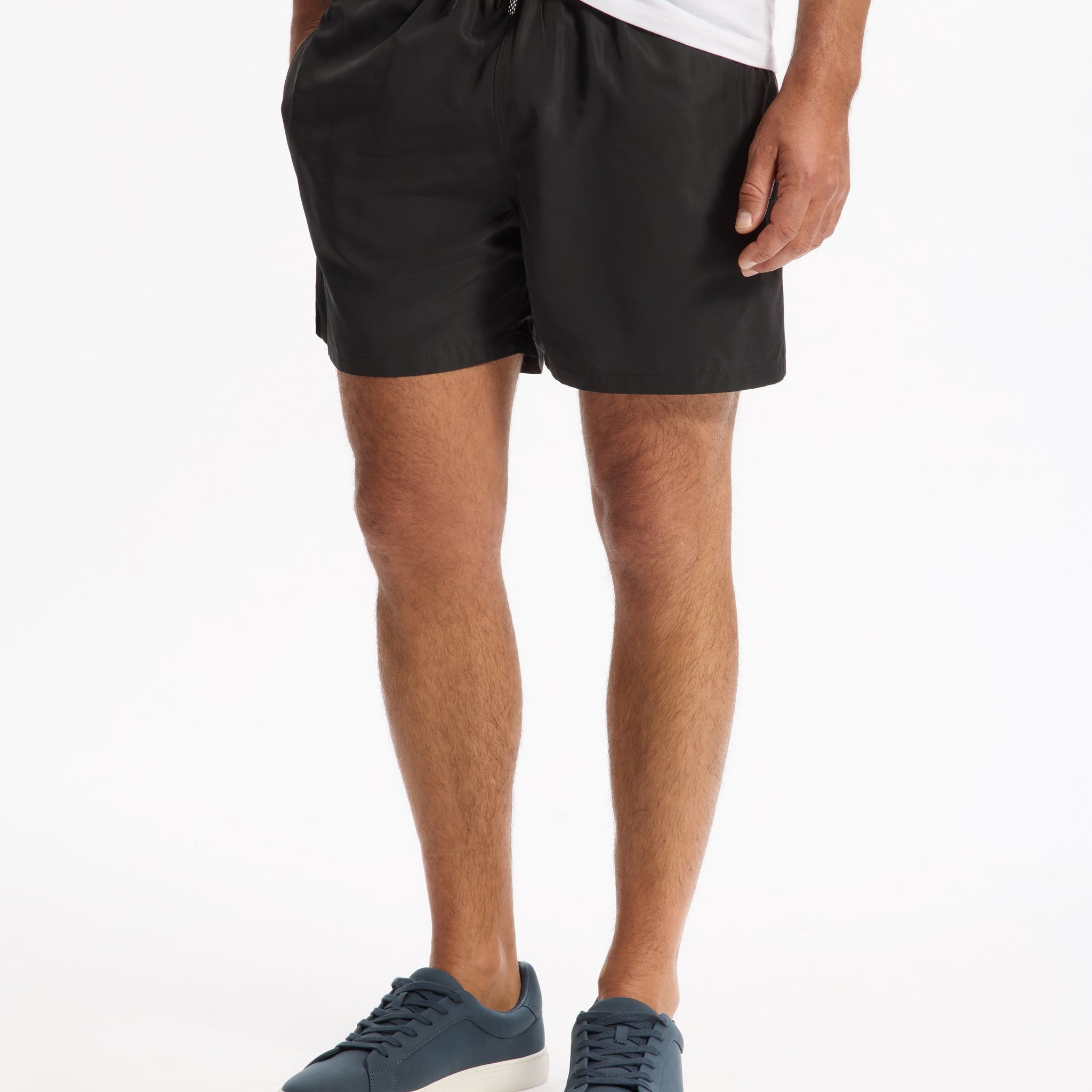 Model wearing black shorts and blue sneakers on a white background