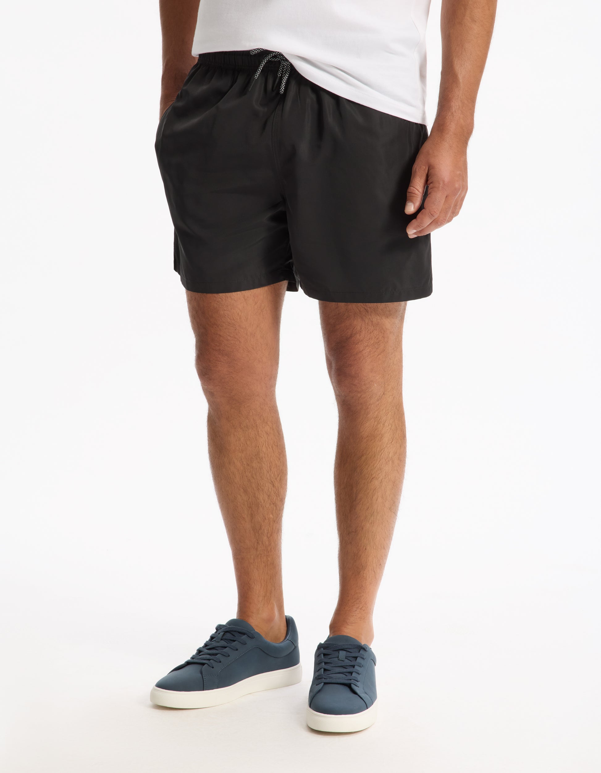 Model wearing black shorts and blue sneakers on a white background