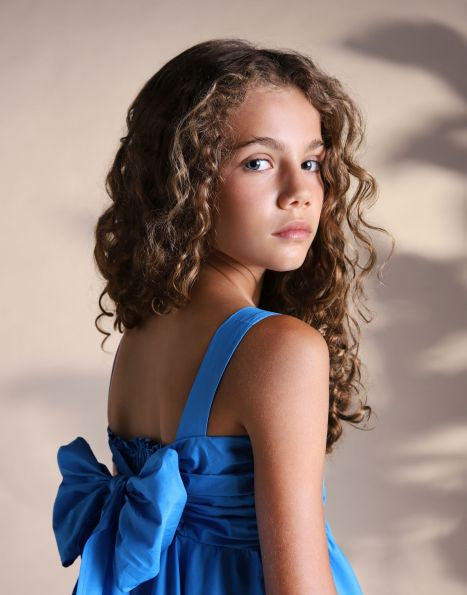 Young girl wearing a khabbaz blue dress with a large bow on a neutral background