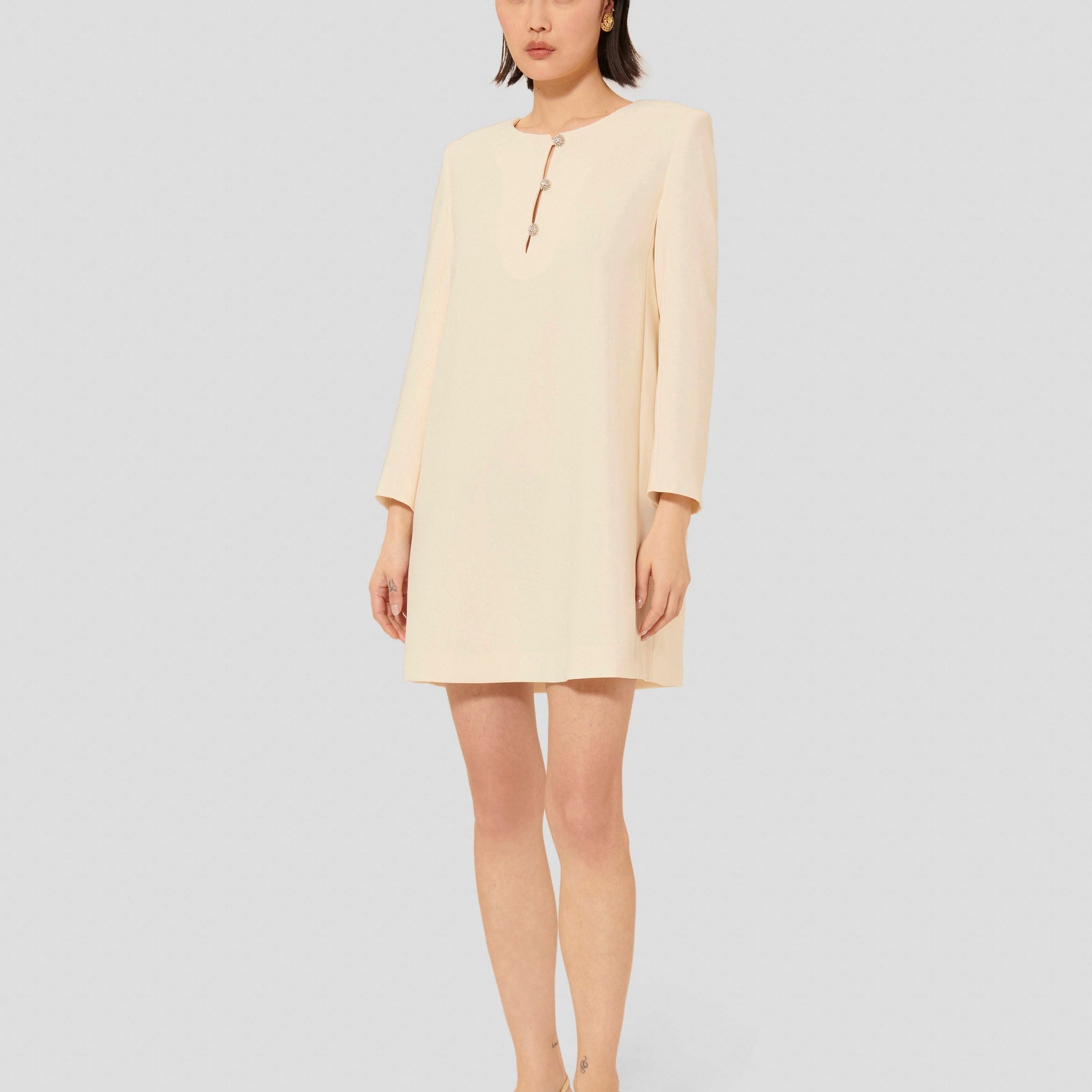 Model wearing Tara Jarmon short ecru crepe dress with long sleeves and a round neckline.