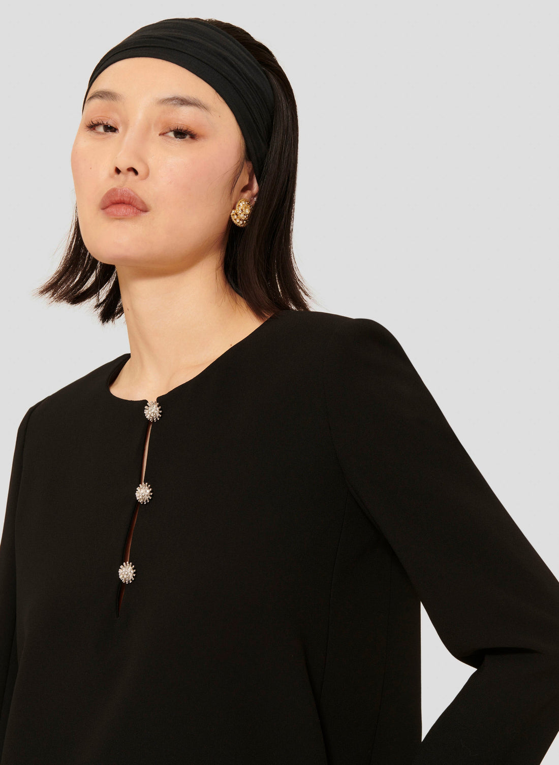 Model wearing Tara Jarmon short black crepe dress with long sleeves and a round neckline.