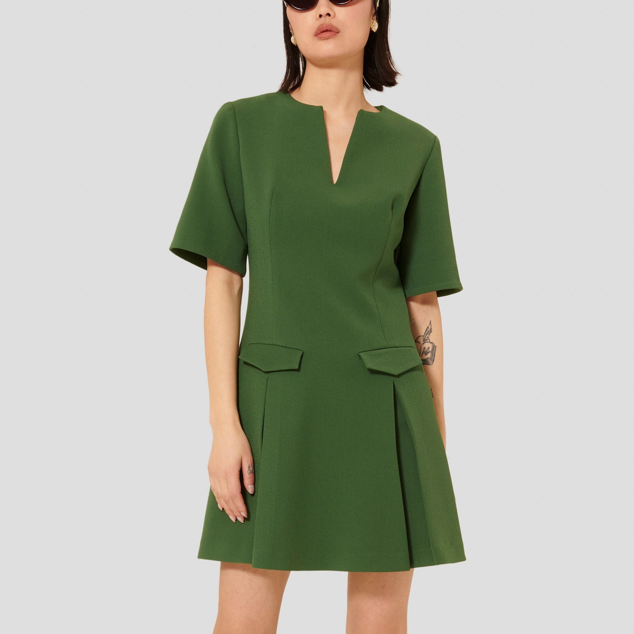 Model wearing Tara Jarmon Green Crepe Short Dress with Pleated Skirt and Flap Pockets.