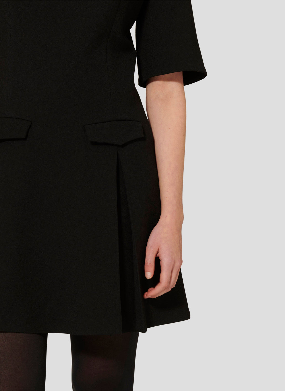 Model wearing Tara Jarmon Black Crepe Short Dress with Pleated Skirt and Flap Pockets.