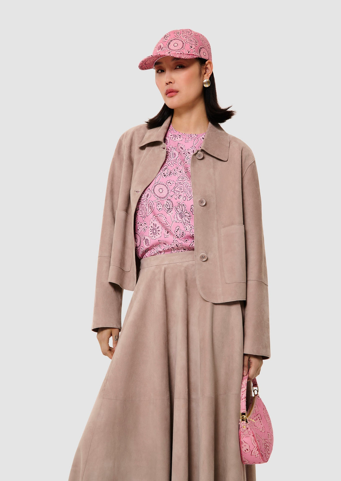 Woman wearing a pink patterned outfit with a beige jacket and skirt, holding a matching pink handbag.