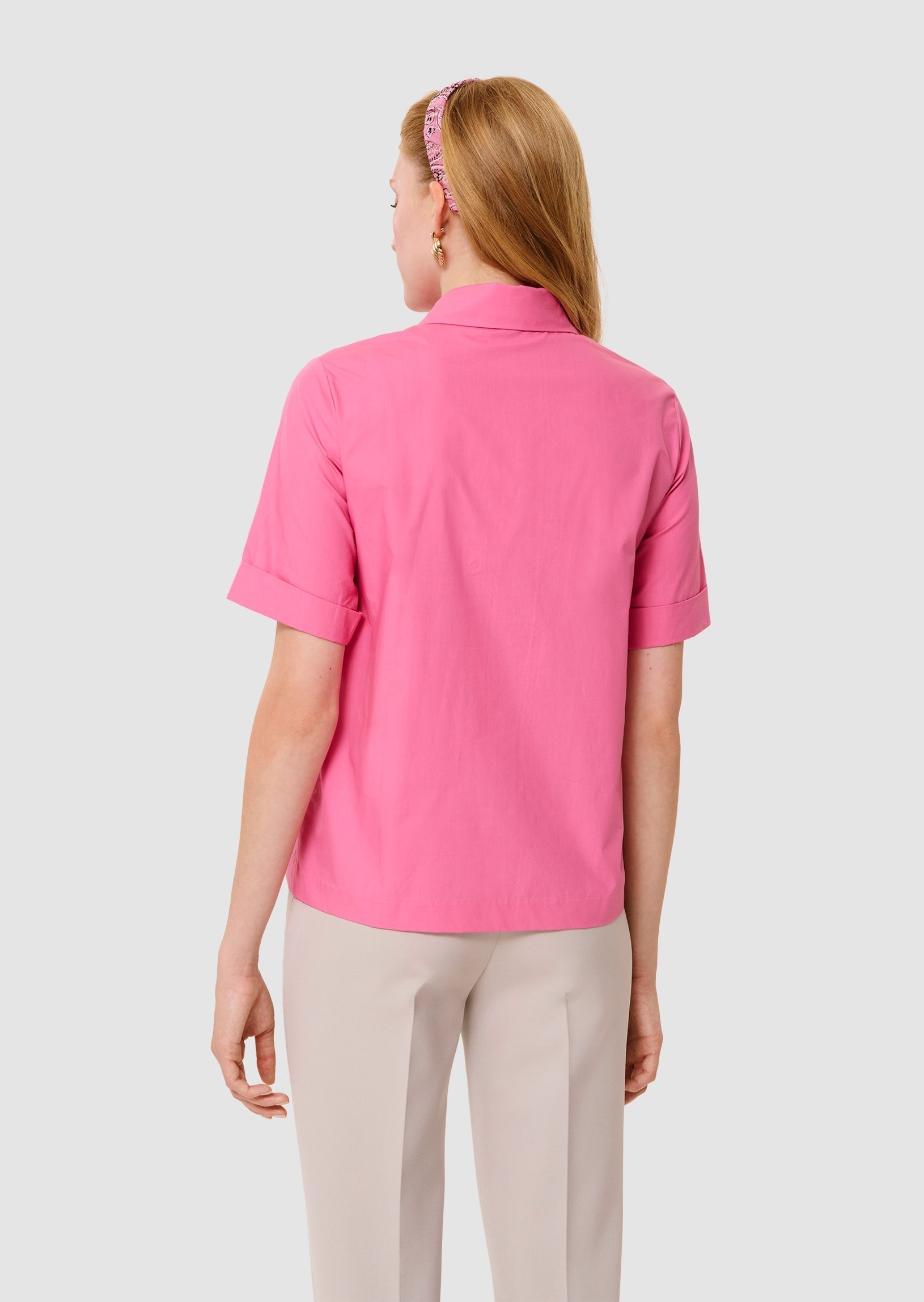 back view of a women wearing a pink blouse with a white background