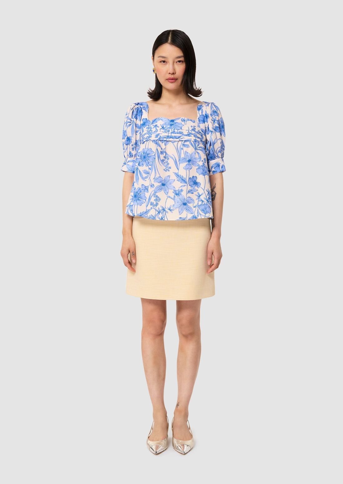 Woman wearing a blue floral blouse and beige skirt on a white background