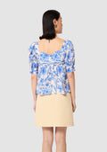 back view of a Woman wearing a blue floral top and beige skirt on a light gray background