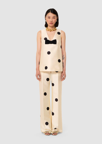 Woman wearing a beige outfit with black polka dots and a bow detail on a light gray background