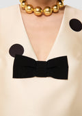 Close-up of a beige garment with a black bow and gold necklace.