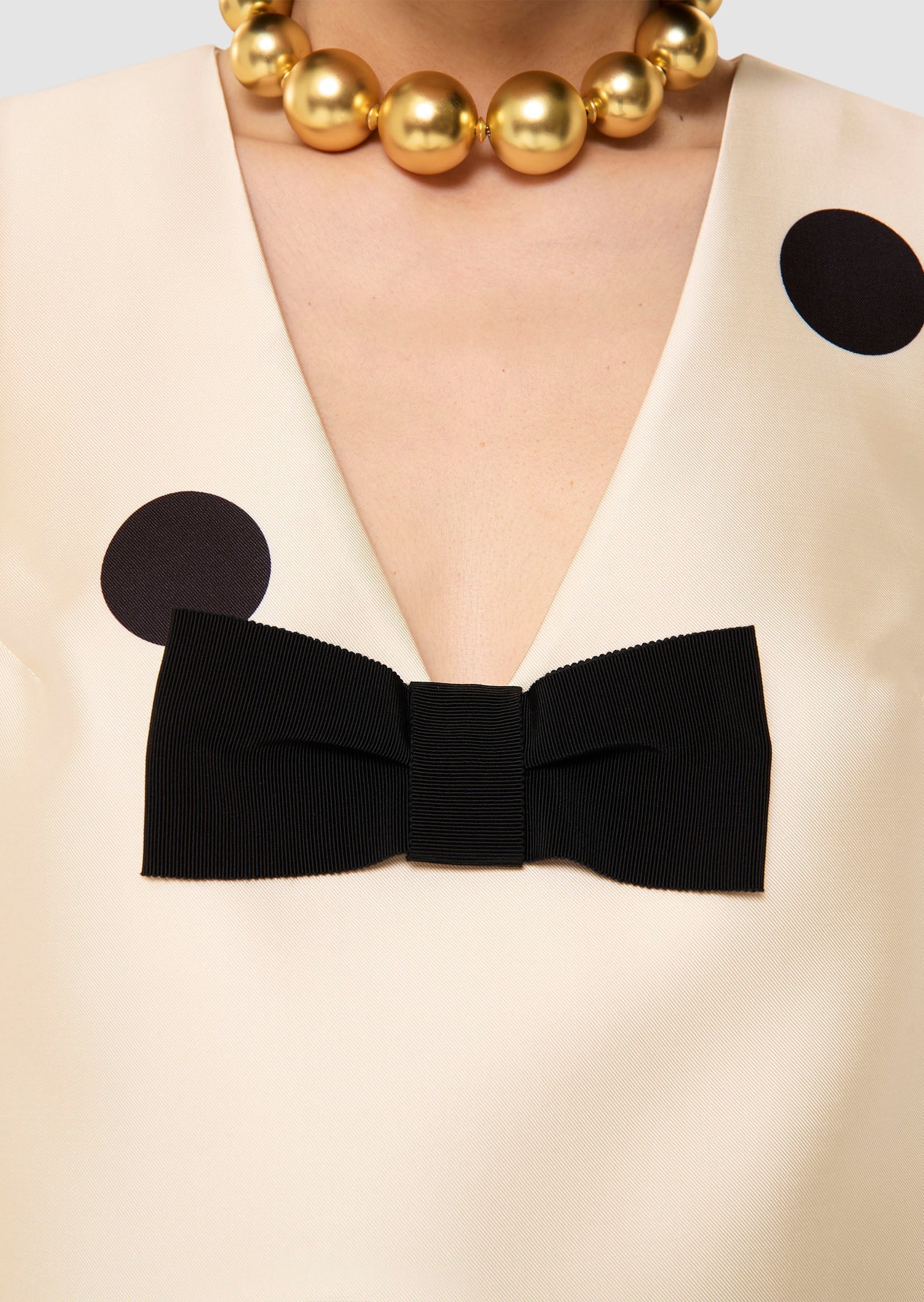 Close-up of a beige garment with a black bow and gold necklace.