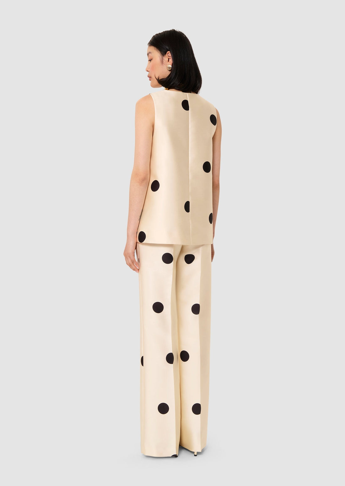 Woman wearing a beige outfit with black polka dots and a bow detail on a light gray background